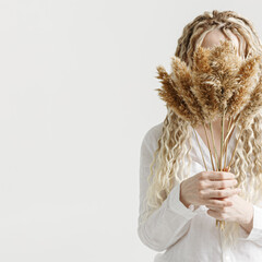 Woman holding pampas grass in front of face, light background, no face trend concept. Female with...