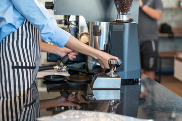 Barita girl grinding coffee and roasting coffee with a coffee machine teaches new employee training in a coffee shop.