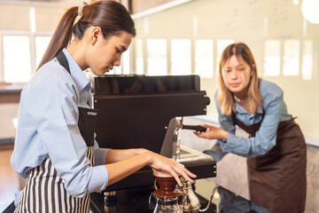 Fototapeta premium Barita girl grinding coffee and roasting coffee with a coffee machine trains new employee training. Two girls take notes at the counter in a coffee shop