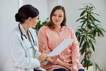 A female nutritionist in a white medical coat consulting a pretty overweight woman.