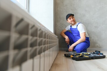 Fototapeta na wymiar young man plumber checking radiator while installing heating system in apartment