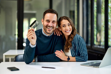 A smiling business couple in love sitting at the office table and using a credit card.