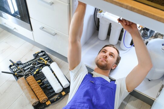 Plumber installs or change water filter. Replacement aqua filter. Repairman installing water filter cartridges in a kitchen. Installation of reverse osmosis water purification system.