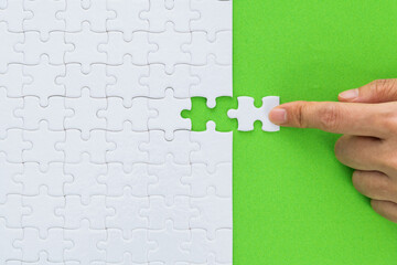 Hand putting the last piece of white jigsaw puzzle