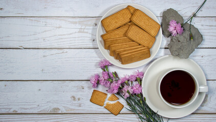 A cup of tea with cookies and flowers on a light table. Romantic breakfast
