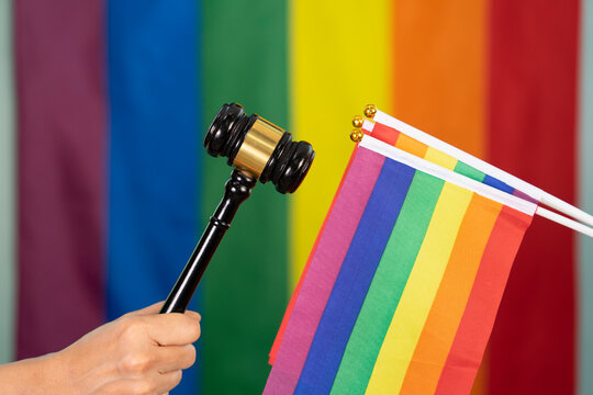 hand of gay pride holding wood gavel or judge hammer, and holding lgbt flags background blurred lgbtq rainbow flag,concept for lgbt claim justice rights of amendment,law,discrimination,equality