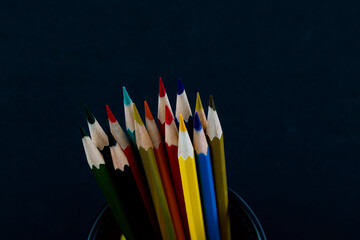 Colorful pencils in metal basket on black background