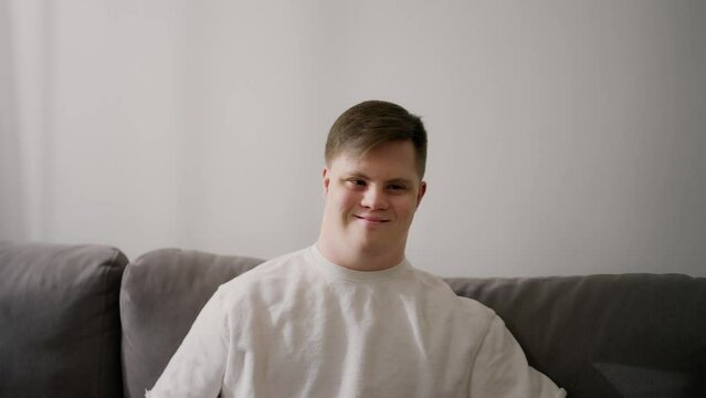 Portrait of happy caucasian man with Down Syndrome sitting on couch at home