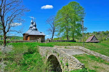 Fototapeta na wymiar Old stone bridge leading to a wooden church in Olchowiec village in summer sunny day, Low Beskids, Poland