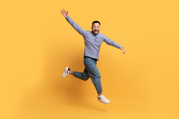 Fototapeta na wymiar Happy Excited Asian Man Jumping In Air On Yellow Background