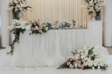 Wedding presidium. Banquet table for newlyweds with flowers, greenery and candles. Lush floral arrangements in vases. Classic wedding.	

