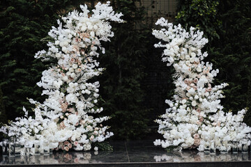Wedding arch decorated by white flowers with greenery standing in the center of wedding ceremony in garden beautiful.	