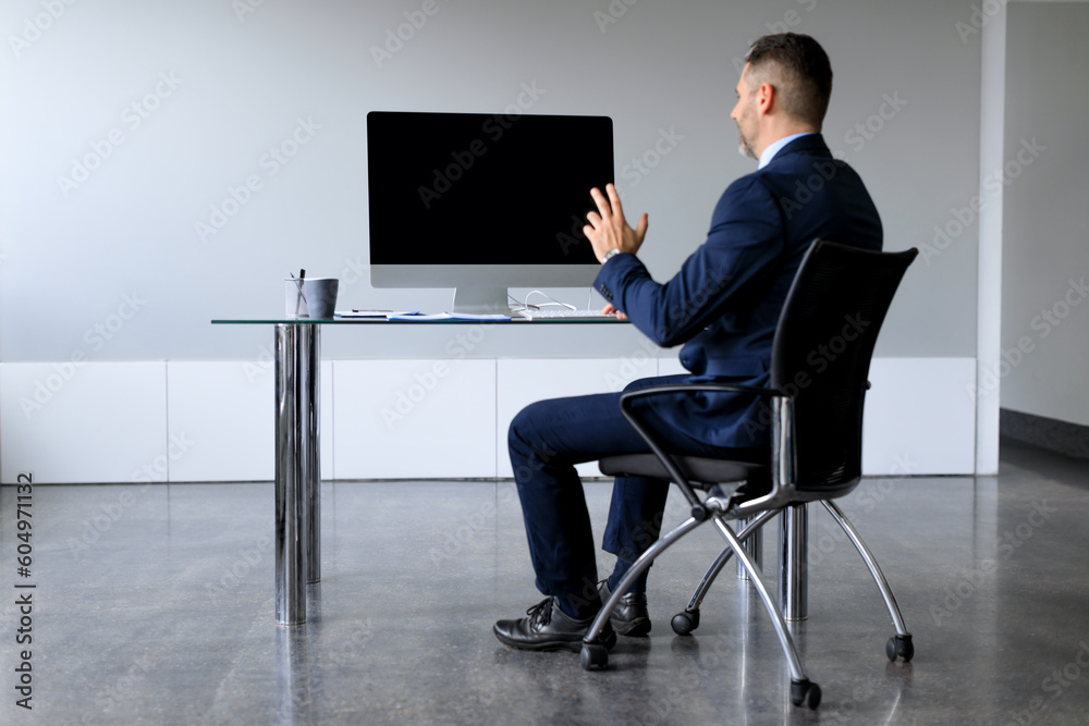 Poster Rear view of middle aged businessman looking at blank empty computer monitor, having online web video call in office