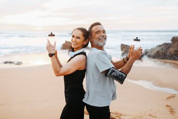 Happy mature caucasian man and woman in sportswear with phone, bottles of water have fun in morning - obrazy, fototapety, plakaty