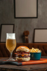 Tasty hamburger with potato chips and beer on the table on the cafe with empty frames background. Fast food concept.
