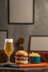 Tasty hamburger with potato chips and beer on the table on the cafe with empty frames background. Fast food concept.