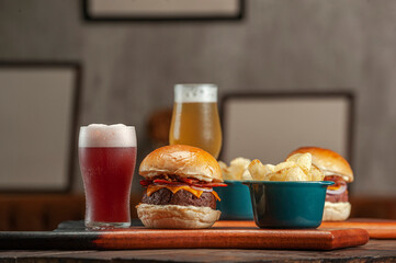 Tasty hamburger with potato chips and beer on the table on the cafe with empty frames background. Fast food concept.