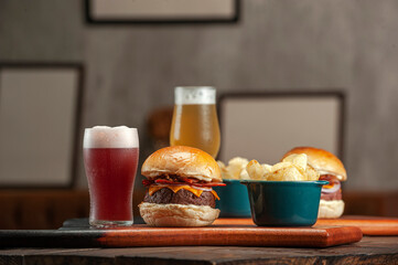 Tasty hamburger with potato chips and beer on the table on the cafe with empty frames background. Fast food concept.