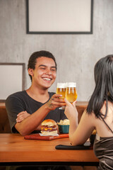 Happy couple toasting with beer at pub restaurant fast food table with burger.