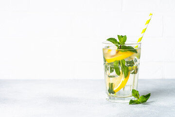 Lemonade in glass on white table. Cold summer drink with ice.