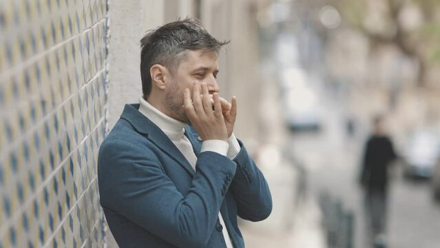 A man stands against the wall and plays the harmonica in the street