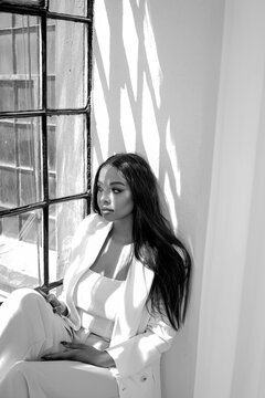 Elegant, fashionable young woman with long hair sitting near the window, relaxing during work day.  Mental health and work life balance concept.