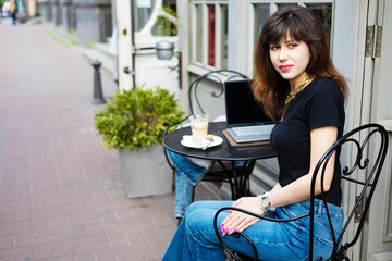 Young woman, digital nomad working remotely from a cafe, drinking coffee and using laptop.