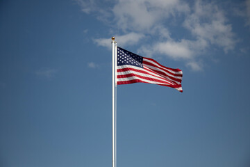 American flag displayed on flagpole with blue sky background on a breezy day.