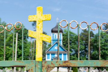 Orthodox cross isolated. Cementry in the background. Old, rusty metal faith symbol. East of Poland. Rusty metal gate. Orthodox wooden church. Countryside small church made of blue wood.