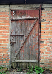 Dilapidated wooden door with red peeling paint in a red brick wall