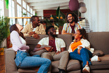 Five multiracial young people talking while resting in living room.