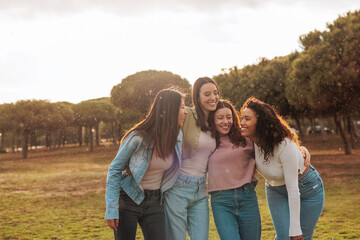 Group of four multiracial girl friends hugging and laughing while standing outside.