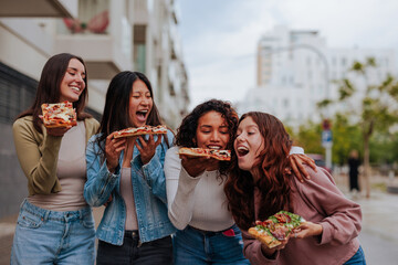 Four young girl friends having pizza while walking on street.