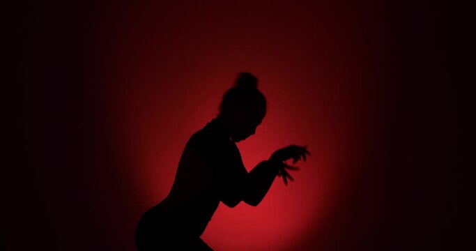 creativity of contemporary dance as a curly-haired woman performs in silhouette. Shot on striking red background, she moves with precision and passion, expressing herself through artful choreography.