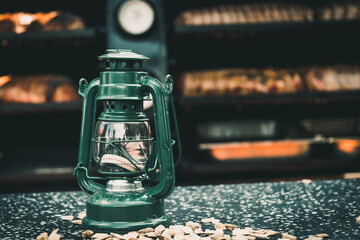 Dark green vintage petroleum lantern as decoration at a market stall at a street festival, a barbecue smoker in the background