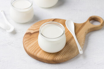 Natural homemade yogurt in a glass jar on a wooden board on a light gray background