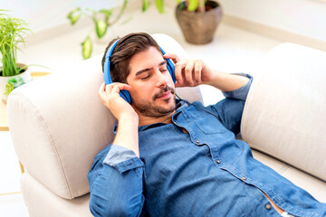 Relaxed man with headphone wearing casual clothes and lying on the sofa at home