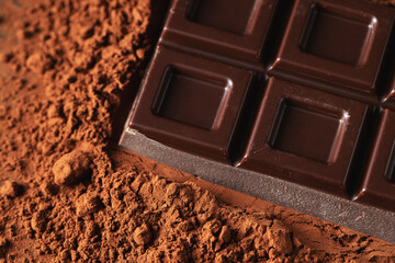 Dark and milk chocolate with nuts on a dark background sprinkled with cocoa powder.