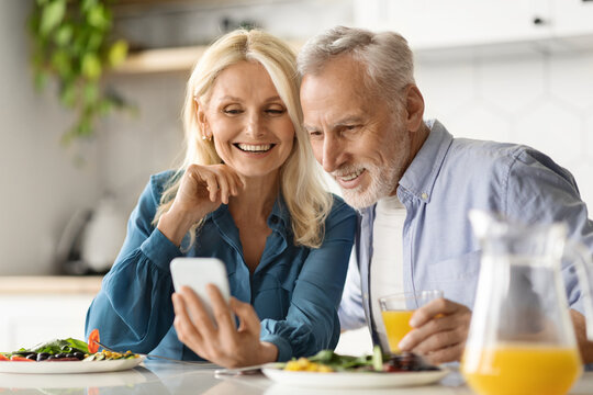 Happy senior couple using smartphone while having breakfast at kitchen - Powered by Adobe