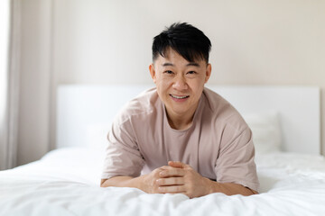 Obraz na płótnie Canvas Portrait of happy handsome chinese man lying on bed