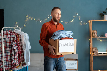 Young man holding a donation box with clothing in his home. Clothes donation or recycling concept