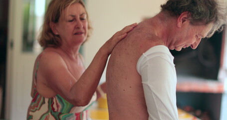 Wife applying sunscreen to husband back. Candid senior couple together putting sunblock prevention