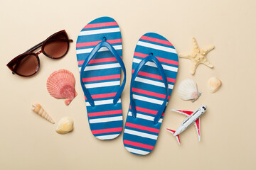 Flip flops with sunglasses and airplane on color background, top view