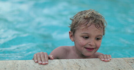 Toddler child at swimming pool lifting body out of water. Kid plays inside pool during summer season