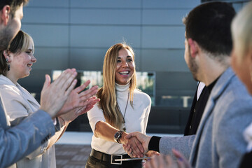group of business people applauding and showing their appreciation to a successful businesswoman who, with a radiant smile, shakes hands with one of them