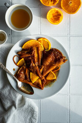 Three crepes suzette with sauce and orange slices on white plate on white tile surface.