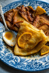 Three crepes suzette in sauce in vintage blue plate on linen tablecloth.