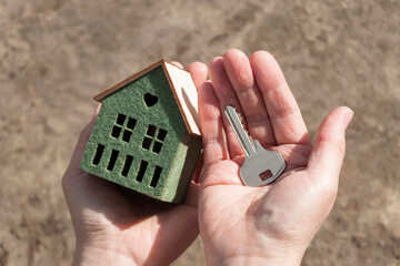 A small house model and a key in female hands on the brown background, selective focus.	