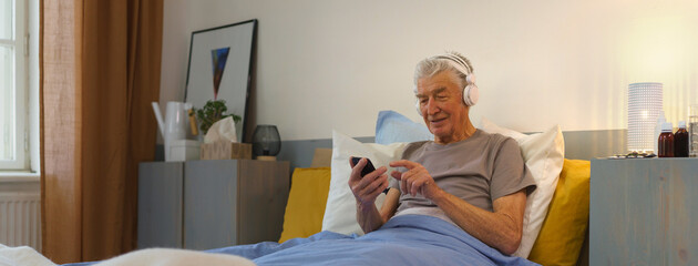 Senior man lying in bed and enjoying music trough headphones.