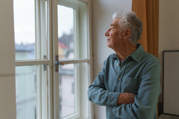 Senior man looking out of window, concept of solitude in retirement.